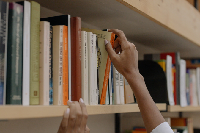a hand selecting a book from a library shelf