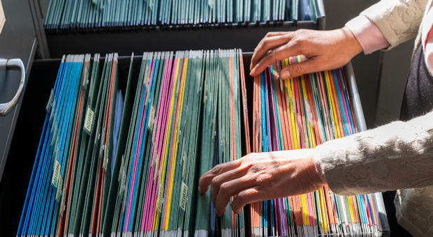 Woman searching a series of documents in a filing cabinet. Another cabinet is open next to it.