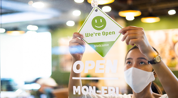 woman in restaurant door hanging up a door sign that says'we are open, welcome'