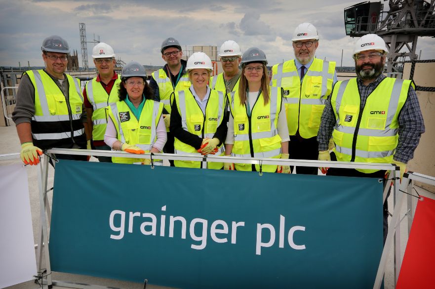 A photo of the GMI group holding a banner that says 'grainger plc' as they celebrate the Topping out stage of the Becketwell development. 