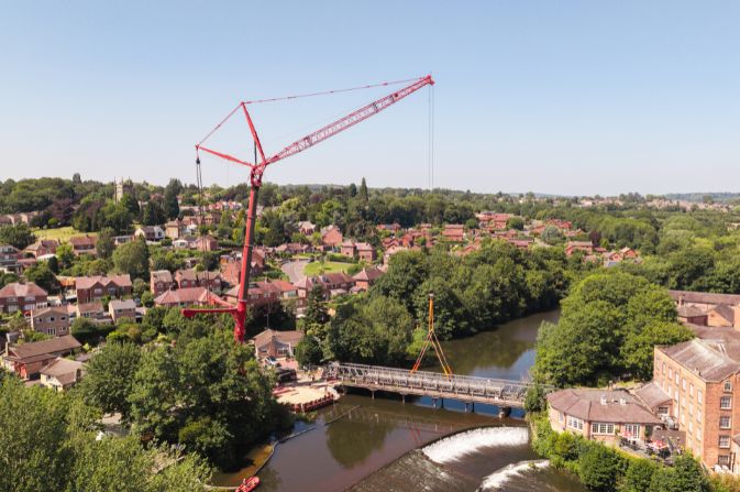 A large red crane lifting a bridge over a river.
