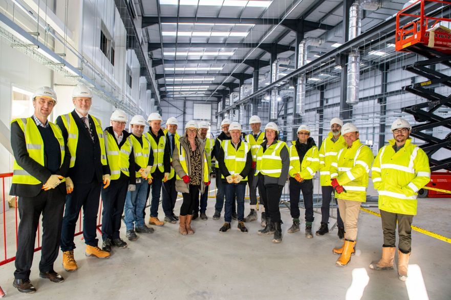 Group of people in high vis jackets and hardhats inside large warehouse.