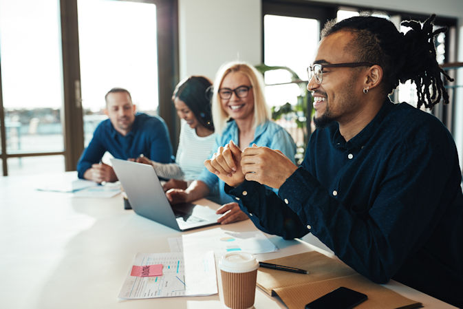 Mixed group of young people at a desk with a laptop smiling