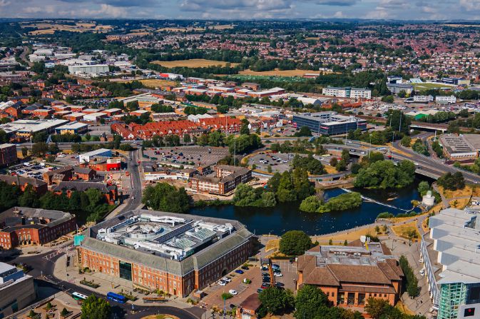 Aerial shot of a city with a large municipal building in the foreground, a river in the centre, and a mix of residential and industrial land.