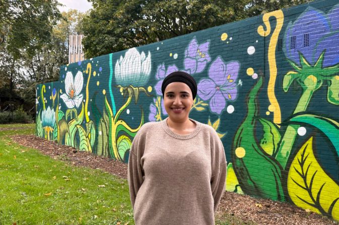 Councillor Gurkiran Kaur standing in front of a colourful floral mural