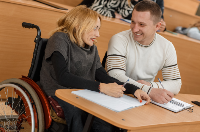 a young woman in a wheelchair sits learning with a young man