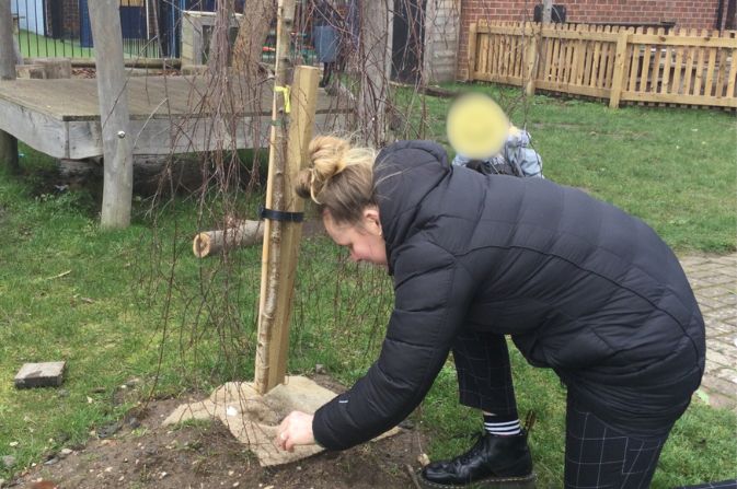 Woman and child planting a tree in the ground.