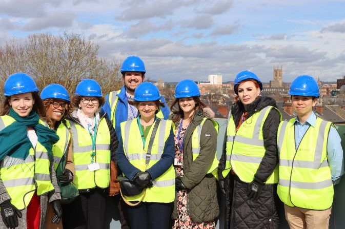 A smiling group of people in hard hats and hhigh vis jackets celebrate the toppigng out of a school building project