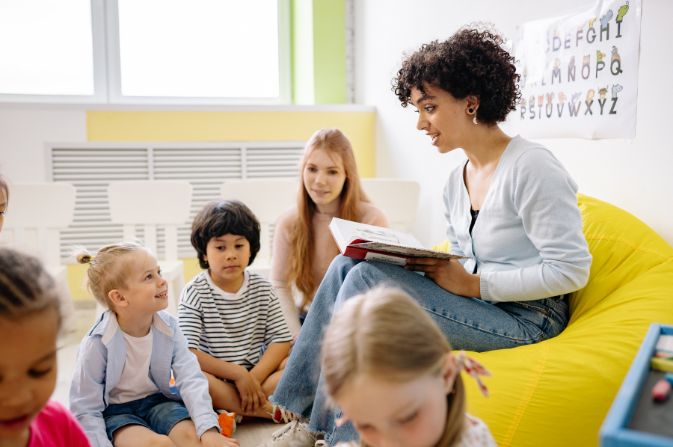 A group of children sit listening to an adult reading from a book