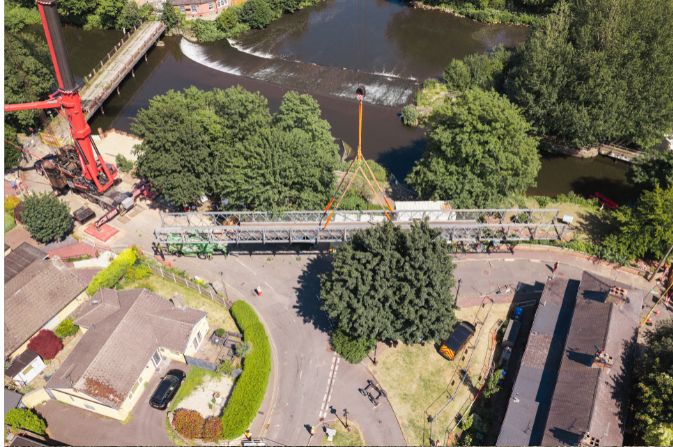 aerial shot of a bridge being lifted by a crane near a river.