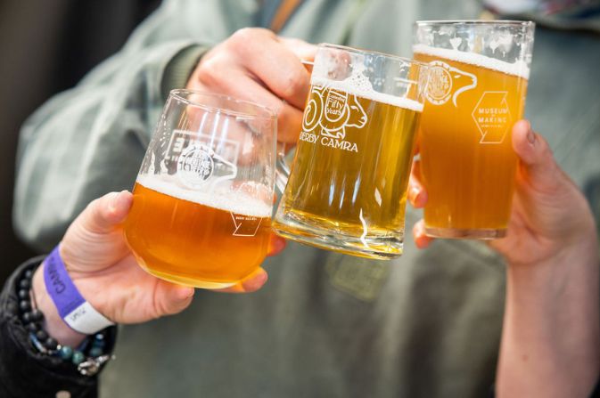 A close up of three people holding beer glasses in a 'cheers' motion