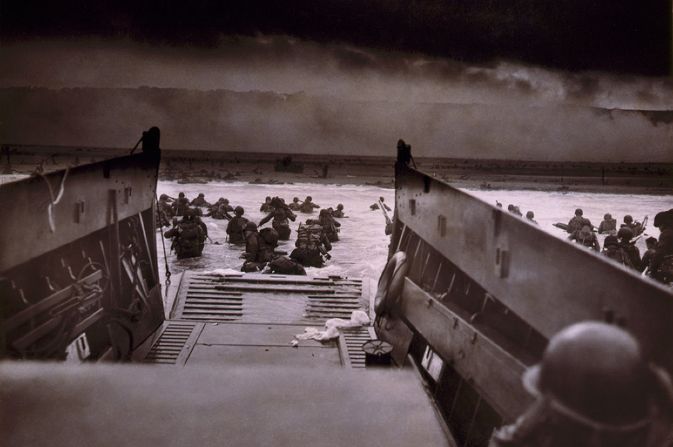 large group of soldiers leaving boat and wading through sea towards beach.