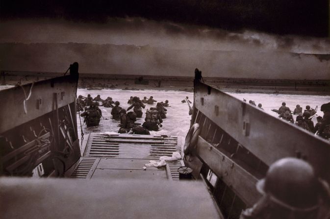 large group of soldiers leaving boat and wading through sea towards beach.
