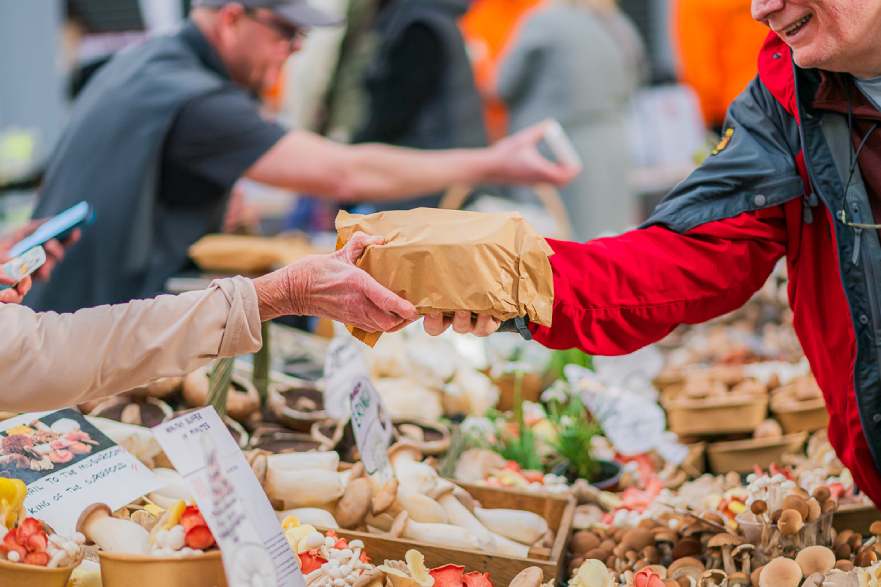 Vendor hands a package to a customer across a colourful market stall