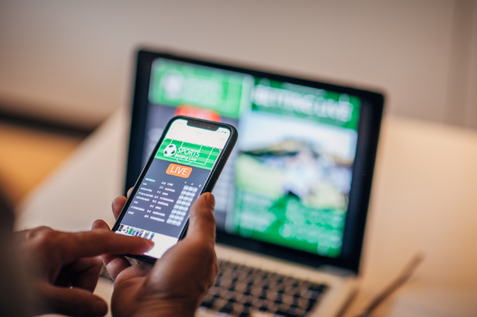 An online gambling site displayed on a mobile phone, with a laptop in the background