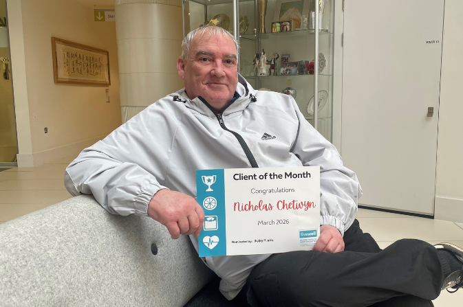 A smiling man sits on a sofa holding a certificate