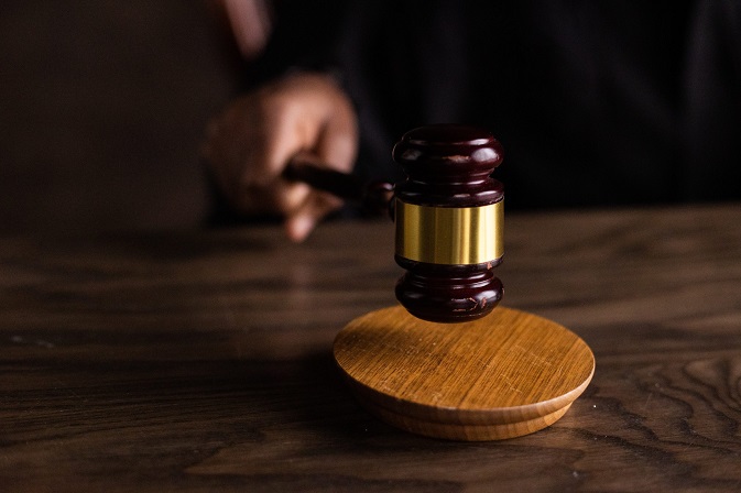 A hand holding an auctioneers hammer, about to bring it down on a wooden plaque to indicate a sale