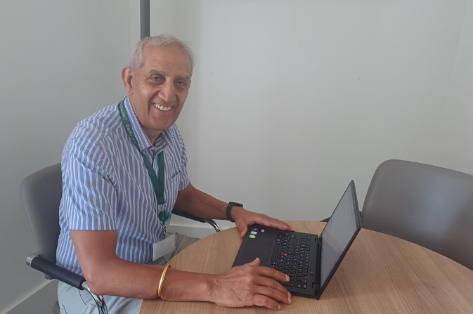 Councillor Dhindsa sitting at a desk with his laptop, smiling