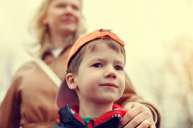Boy in a hat with a woman behind with a reassuring hand on his shoulder