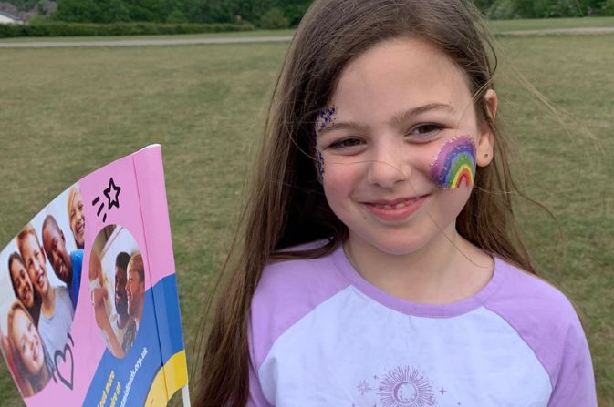 Girl holding a flag and has her face painted at fostering event