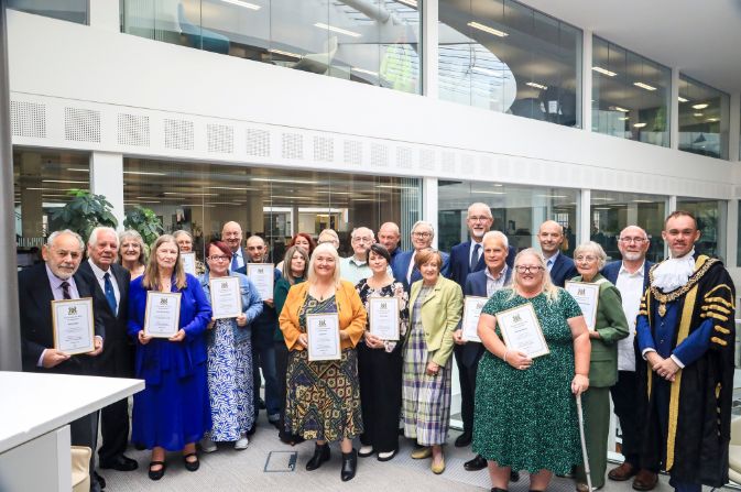 A group of people in formal clothing all holding certificates and smiling at the camera.