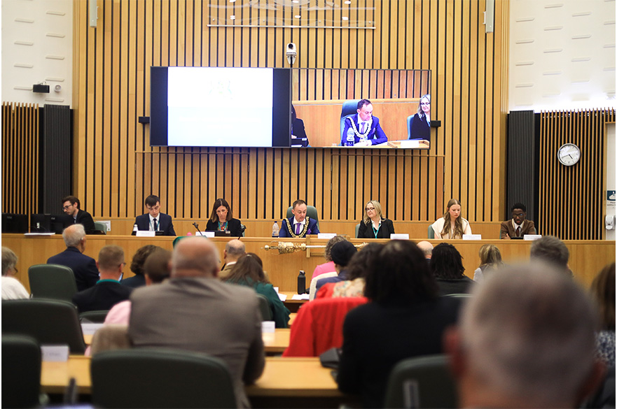 A group of people sat behind the front bench of a large auditorium.