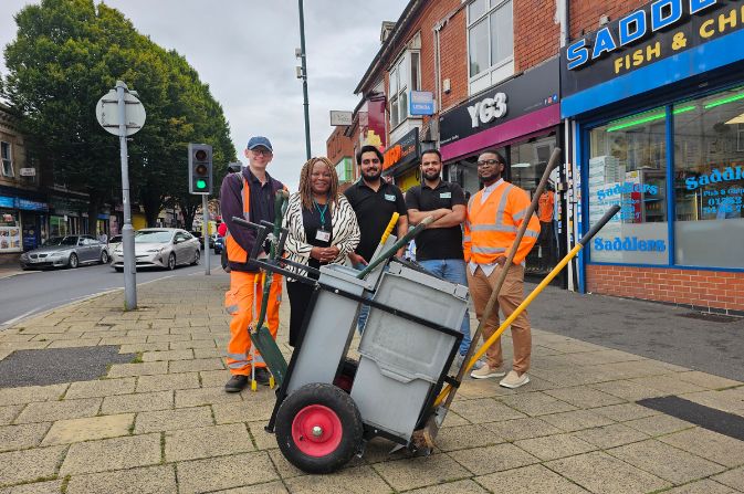a group of people on a street with a wheel barrow in front of them