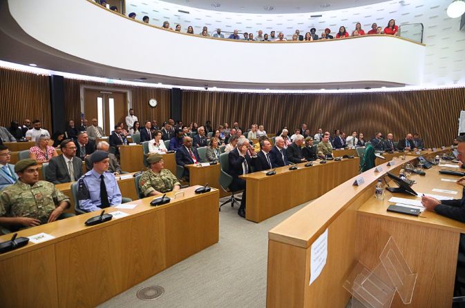 A large assembly hall with people sat behind rows of desks and in a gallery.