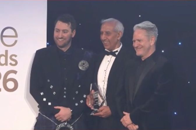 Three people standing on stage as an award is handed out