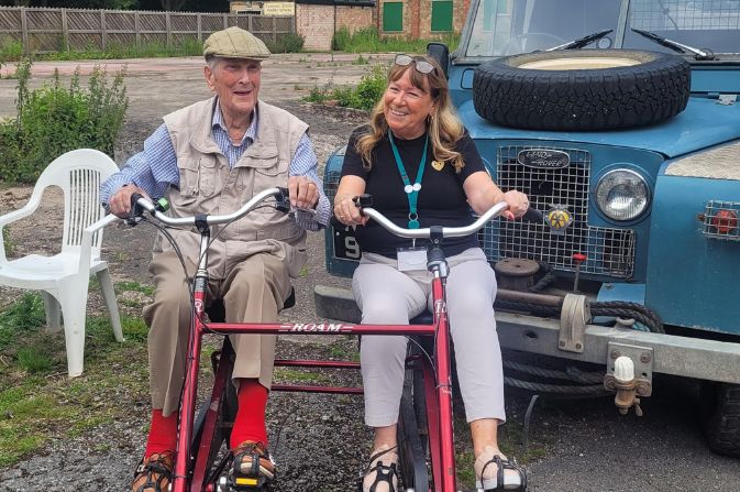 An elderly man and a middle aged woman on a side-by-side bicycle.