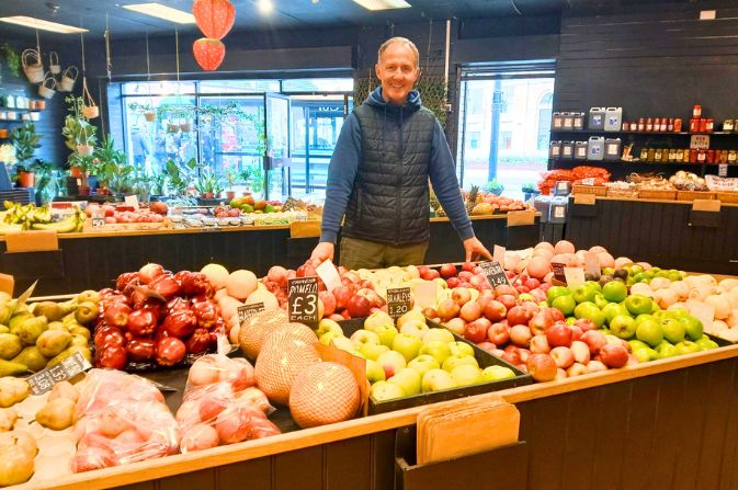A smiling man David Martin stands behind a counter full of colourful fruit and vegetables