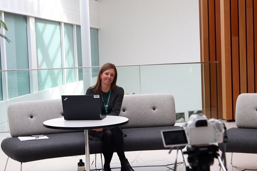 Emily Feenan sitting on a sofa looking talking to a white camera.