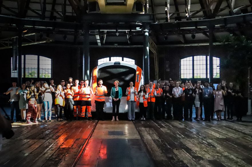 Wendy Morton MP with a large group of young people in orange high vis jackets, stood in front of a train cab.