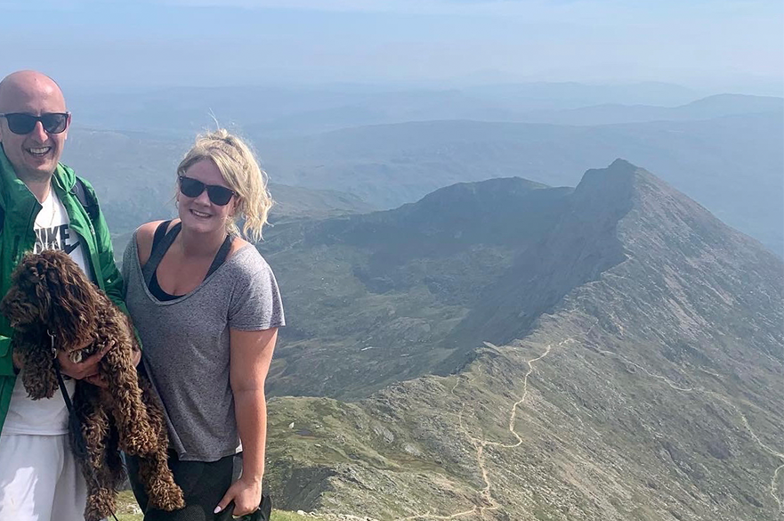 Marie Cheetham standing on a mountain with her partner and dog