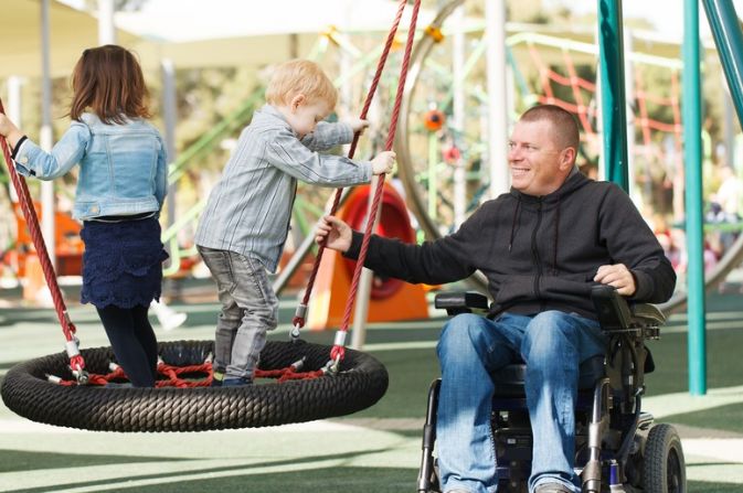 Children on a playground with a man in a wheelchair