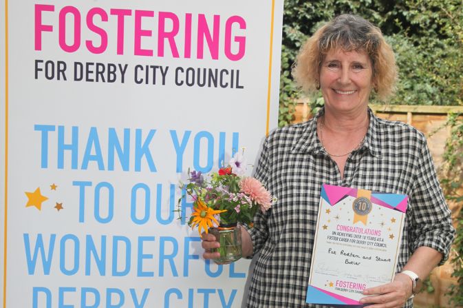 Foster carer Pat holding flowers and a certificate for long service recognition