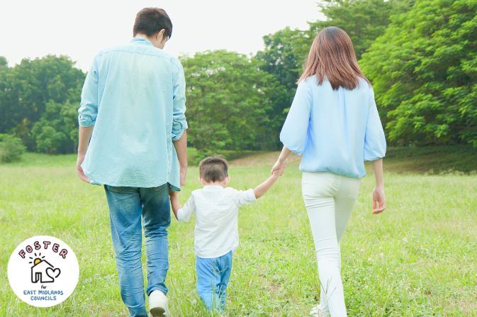 Two adults walking with a child holding hands in a field.
