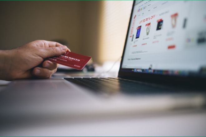 Person holding credit card near laptop.