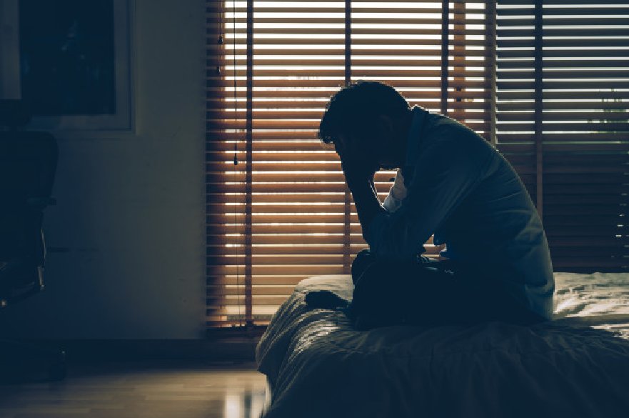 Man sat on bed with head in hands in the dark