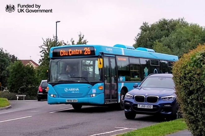 Blue bus driving along road. Funded by UK Government logo.