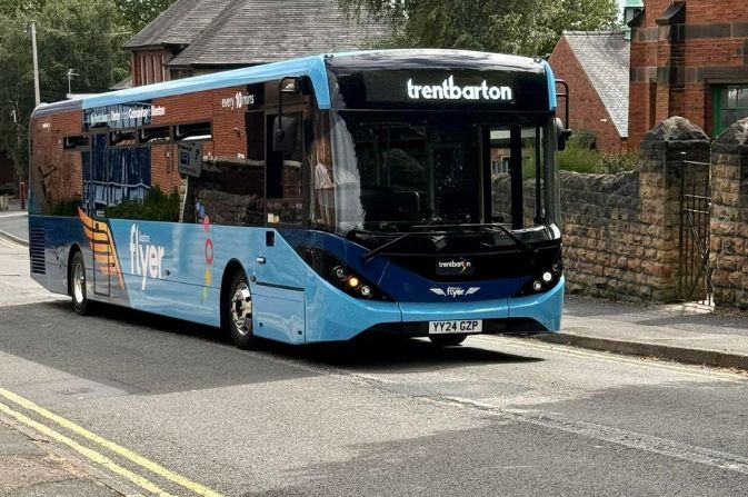 Blue single decker bus travelling on road. It has Ilkeston Flyer branding on it.