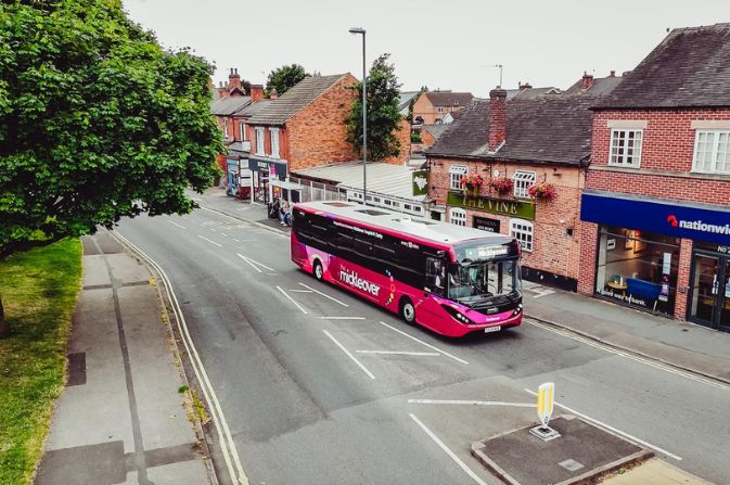 Pink Mickleover bus driving along a high street.