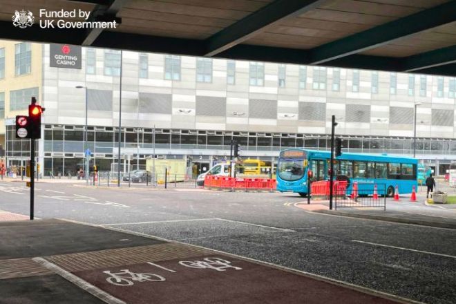 blue bus at traffic lights. a new red-paved cycle lane is in the foreground. Funded by UK Government