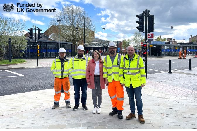 four men in high visibility jackets with lady in pink coat outside Derby Railway Station